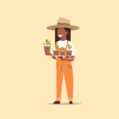 female farmer holding potted plants african american woman in uniform planting young seedlings in garden agricultural worker eco farming concept flat full length
