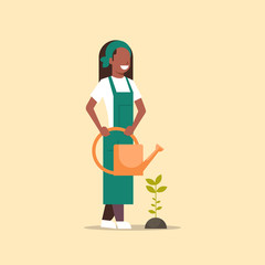 female farmer growing seedling plant flower or vegetable african american woman holding watering can gardener in uniform agricultural eco farming concept flat full length