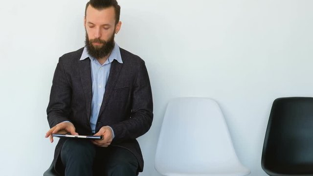 Business guy waiting for appointment. Young bearded man sitting looking through documents. Annual report in hands.