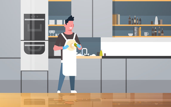 young man washing dishes guy wiping plates doing housework dishwashing concept modern kitchen interior flat horizontal full length