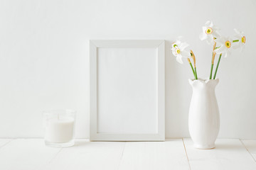 Mockup with a white frame and white daffodils in a vase on a white wooden table
