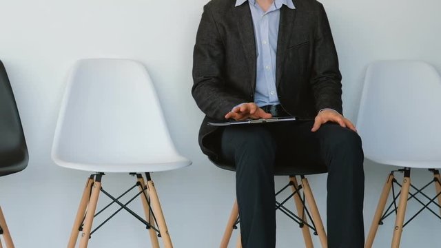 Business guy waiting for appointment. Anxious and fidgety. Fingers tapping on folder with financial report documents.