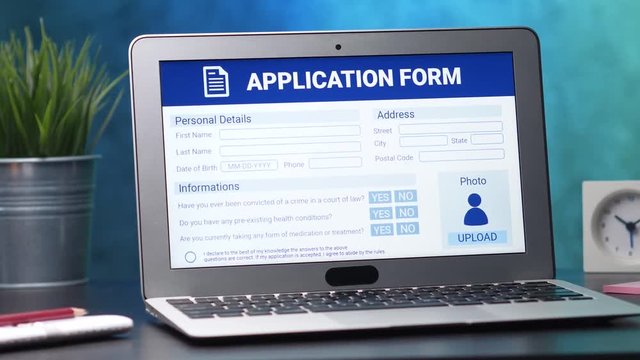 Laptop computer with an application form on its display. Camera turning slowly around the desk.