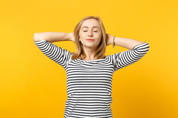 Relaxed young woman in striped clothes keeping eyes closed sleeping with hands behind head isolated on yellow orange wall background. People sincere emotions, lifestyle concept. Mock up copy space.