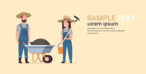 gardener man with wheelbarrow of earth woman holding hoe and bucket couple farmers planting plants flowers and vegetables working in garden gardening concept full length copy space horizontal