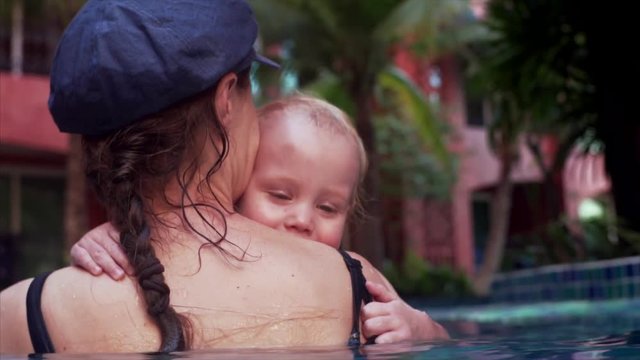 Mom plays with her beloved son bouncing in the pool making him to smile sweetly, slow motion. Pattaya, Thailand. 