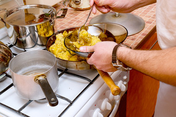 A man in the kitchen puts roast potatoes in a plate