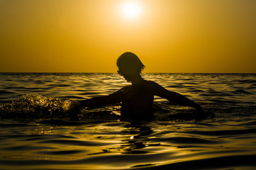 Fototapeta na wymiar Girl swimming in the sea at sunset, splashes of transparency water, female black silhouette