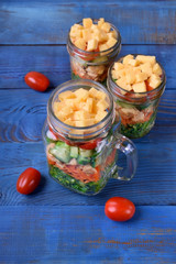 Layered salad with cheese, kale, carrot, chicken, cucumbers and cherry tomatoes in glass mason jar