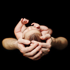 Father's hand and newborn baby on black background