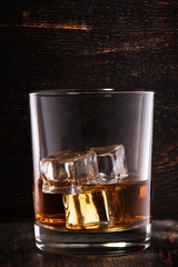 Whiskey with ice in glasses, rustic wood background.
