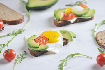 Toasts with avocado, cherry tomato and fried egg. The composition is supplemented with arugula greens. Light background. 