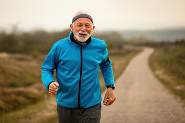 Motivated mature athlete jogging and listening music on earphones.