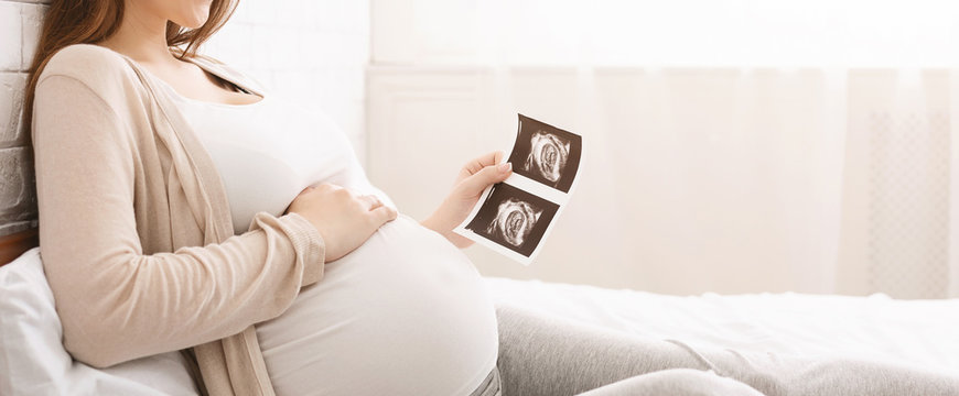 Pregnant woman holding ultrasound image lying in bed