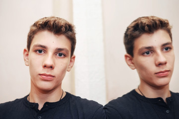 A cute young boy with a serious face standing near the mirror in a restaurant. The mirror reflects the boy