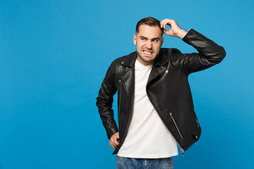 Fototapeta premium Young sad frustrated worried unshaven man in black jacket white t-shirt looking camera isolated on blue wall background studio portrait. People sincere emotions lifestyle concept. Mock up copy space.