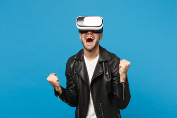 Stylish young unshaven man in black jacket white t-shirt looking in headset, virtual reality vr isolated on blue wall background studio portrait. People emotions lifestyle concept. Mock up copy space.