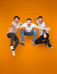 Fototapeta na wymiar Excited friends jumping together over orange background