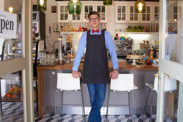 Confident young coffee shop owner man standing in cafe and waiting for guest