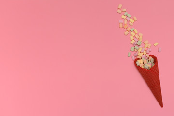 Red waffle ice cream cone. The wallow multi-colored marshmallows isolated on a pink background. Congratulations, celebration concept. Top view. Copy space.