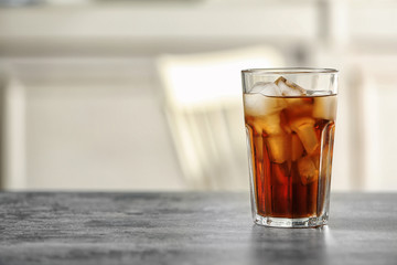 Glass of cola with ice on table against blurred background, space for text