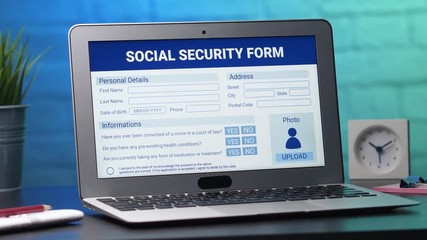 Laptop computer with a social security application form on its display. Camera turning slowly around the desk.