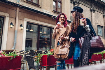 Outdoor shot of young women walking on city street. and having coffee. Friends talking and having fun