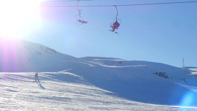 View of moving ski lift with people and sportsmens snowboarding from snowy mountain on background