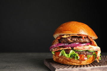 Tasty burger with bacon on table against black background. Space for text - obrazy, fototapety, plakaty