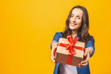Smiling young beautiful woman holds red gift box. Isolated over yellow background. Studio.