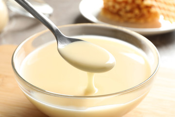 Spoon of pouring condensed milk over bowl on table, closeup. Dairy products