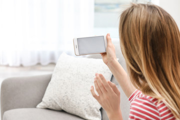 Young woman using video chat on smartphone in living room, closeup. Space for design