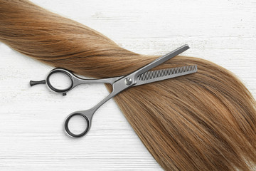 Flat lay composition with light brown hair and thinning scissors on white wooden background. Hairdresser service