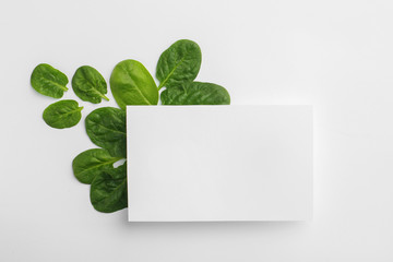 Blank card and fresh spinach leaves isolated on white, top view. Space for text