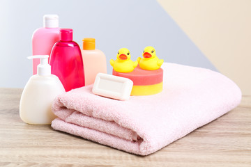 Baby cosmetic products, toys and towel on table against color background