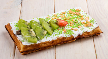 Belgian waffle with cream, strawberries and kiwi. On a light wooden background