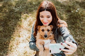 .Pretty young woman playing with her dog in the park outdoors. Taking pictures together doing funny funny faces with her mobile phone. Lifestyle. Dogfriendly.