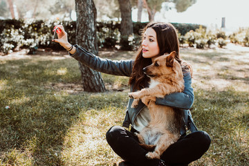 .Pretty young woman playing with her dog in the park outdoors. Taking pictures together doing funny funny faces with her mobile phone. Lifestyle. Dogfriendly.