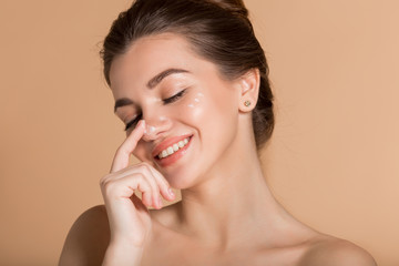 Happy smiling girl with perfect skin with moisturizing face cream on a cheek. Skin care and health...