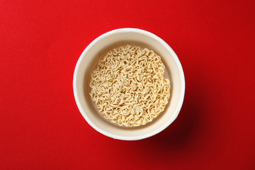 Cup of instant noodles on color background, top view