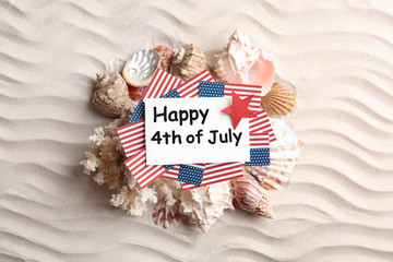 Flat lay composition with greeting card, USA flags and seashells on sand. Happy Independence Day