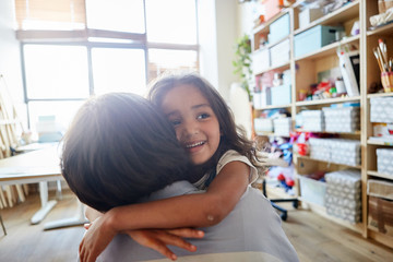 Sweet little girl smiling and embracing young teacher in classroom at art school