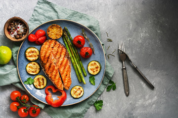 Grilled salmon with vegetables zucchini, asparagus, tomato, sweet pepper on a plate, gray background. Top view, flat lay,copy space
