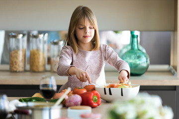 Obraz na płótnie Canvas Beautiful cute little girl preparing salad in a bowl in the kitchen at home.