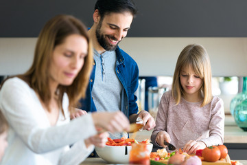 Attractive young man with her little cute daughter making salad together on kitchen at home