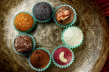 Assorted vegan/raw candy. Round vegan sweets with nuts, coconut flakes, poppy seeds and dried fruits on a beautiful singing bowl. Close up. Flat lay