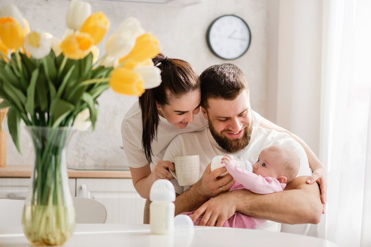 Happy Young Family Feeding Infant In Kitchen