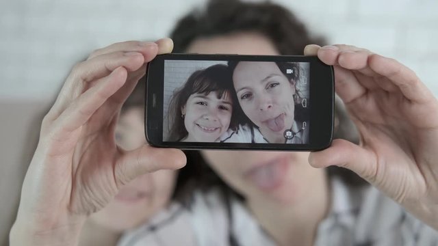 Funny selfie. A woman with a child is grimacing. Funny mother and daughter show tongues for selfie.