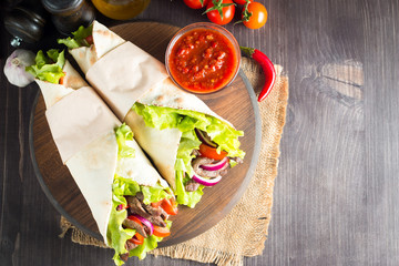 Photo of Mexican sandwich food, burrito, fajita, tacos, wrap made of tortilla, beef, chicken, fresh vegetables on rustic wooden background. Fast food concept. Healthy lunch snack. Copy space. 