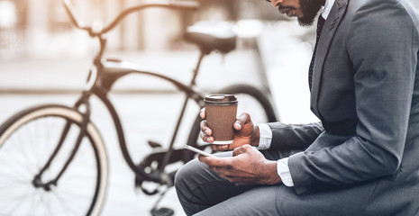Businessman with coffee and smartphone sitting near bike